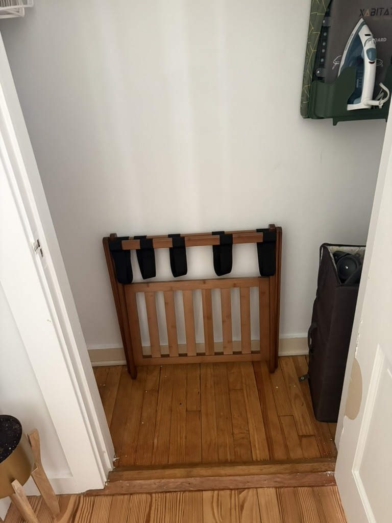 Folded walnut luggage rack stored upright inside a vacation-rental closet