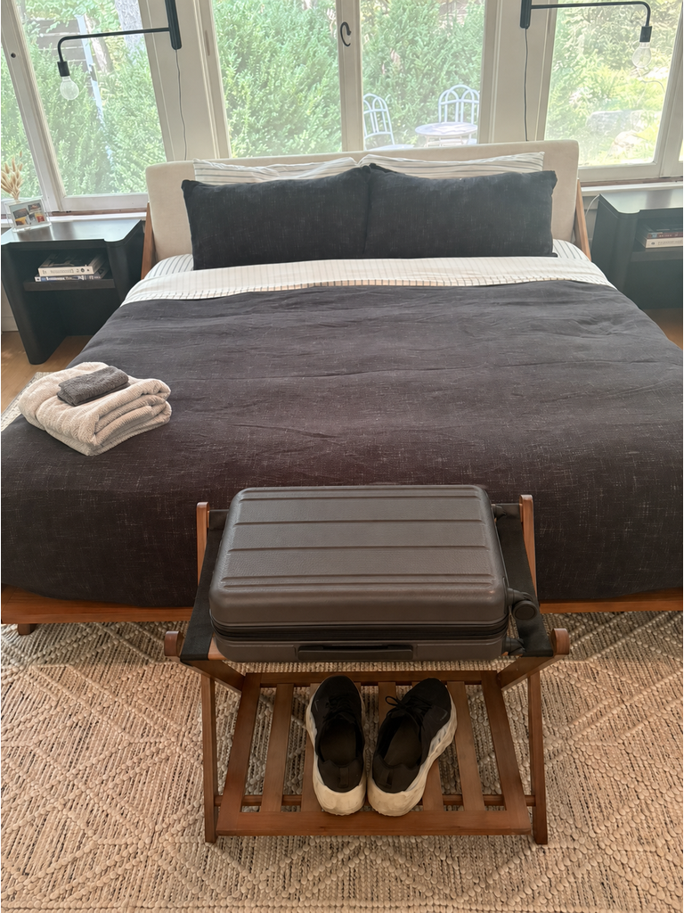 Medium suitcase resting on a walnut luggage rack with shoes stored on the lower shelf